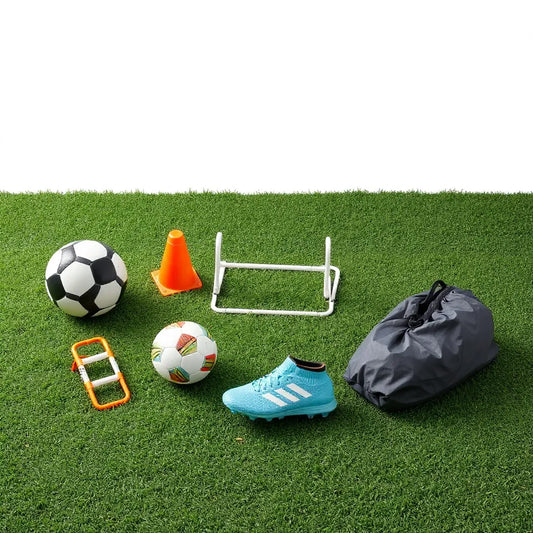 Soccer training gear laid out on turf: cleats, ball, cones, training ladder, and hurdles