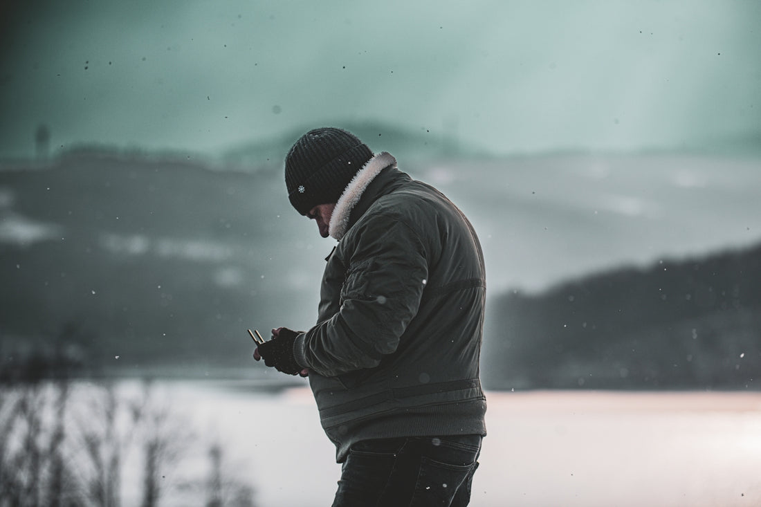 A man standing in the snow looking at his cell phone