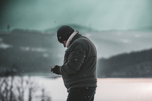 A man standing in the snow looking at his cell phone