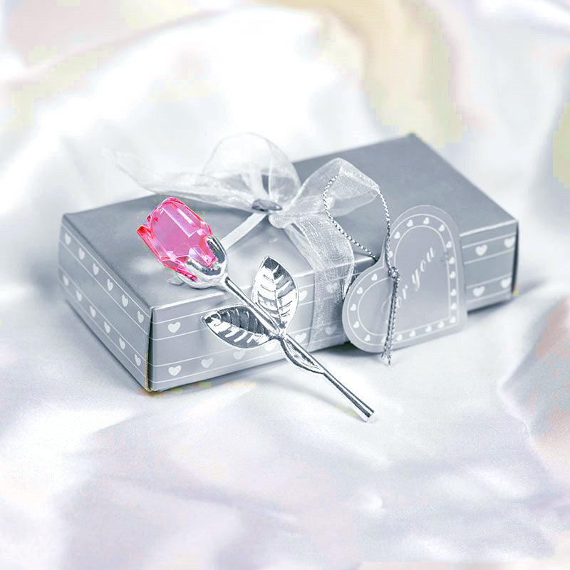 A shimmering silver gift box adorned with a transparent ribbon and a decorative crystal glass rose from https://sammyskfootball.com accompanied by a feather-shaped pen atop satin fabric, perfect as a Valentine's Day gift.