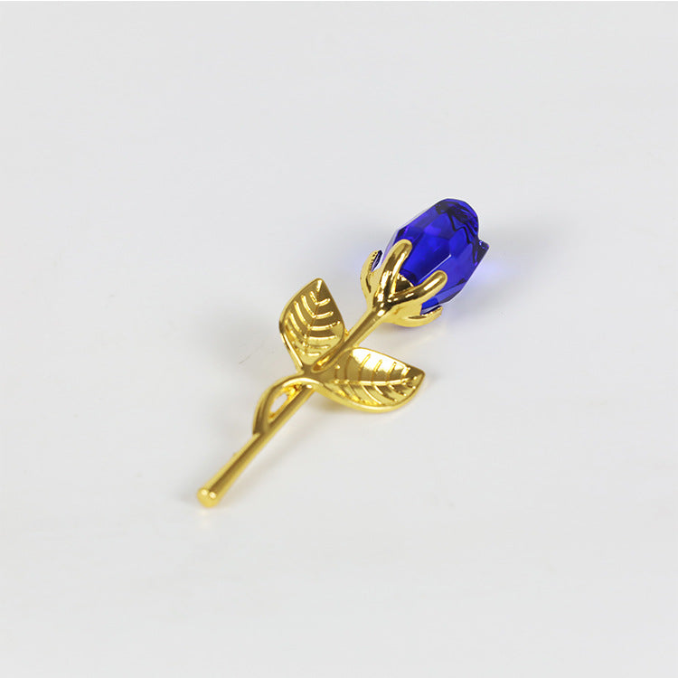 An elegant sapphire-colored crystal glass rose with gold-tone leaves and stem from Sammy's K Football laying against a white background, perfect as a Valentine's Day gift.